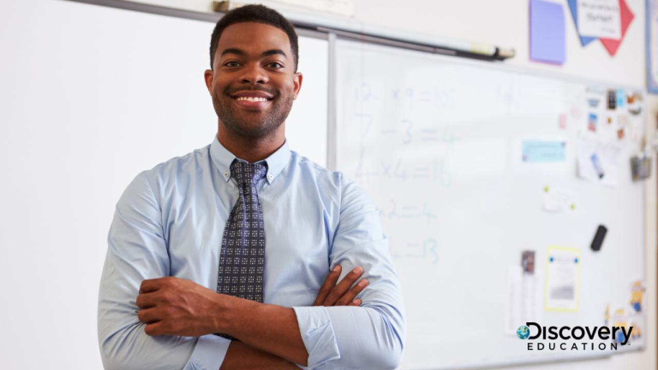 Teacher standing in the front of class with arms crossed, smiling.