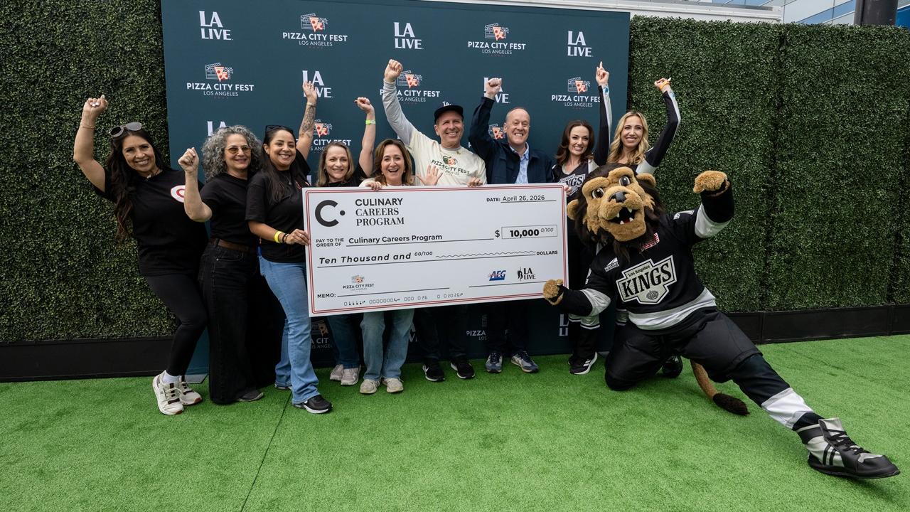 Group stands on a branded step-and-repeat holding a large donation check for the Culinary Careers Program at LA LIVE, with a mascot posing nearby.