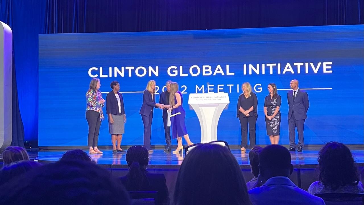 Image of eight people on stage in front of a backdrop that says, "Clinton Global Initiative"