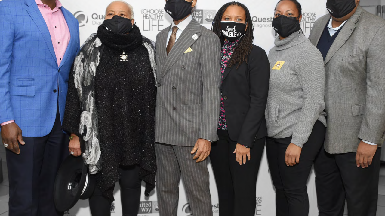 a group of six people stand in front of a wall of logos for choose healthy life, quest diagnostics and united way