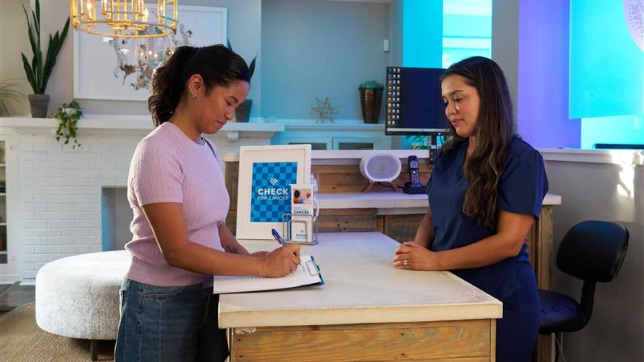 A person filling out a form at a clinic with another person behind a desk.