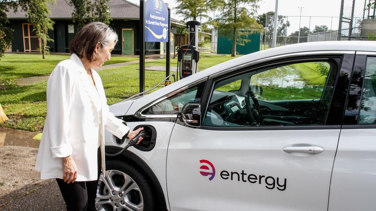 A person using an EV charger for a white car which has the entergy logo on the door 