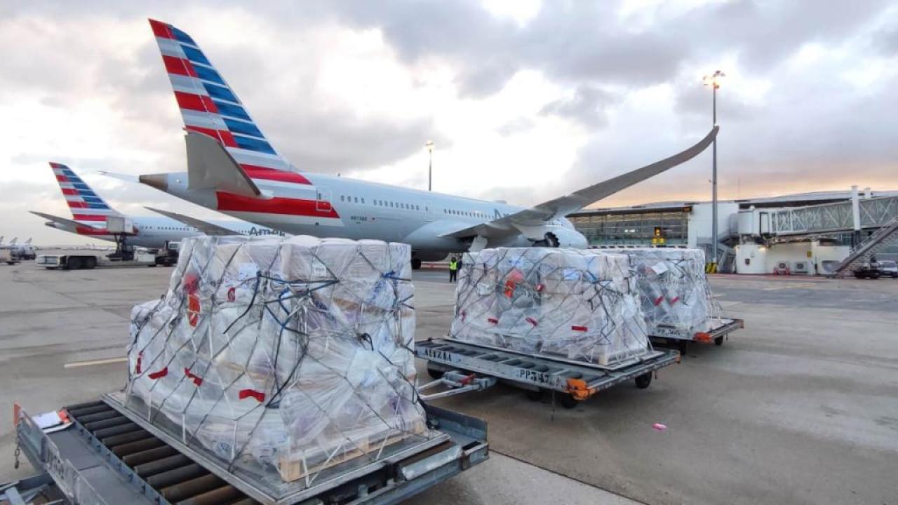 Pallets of cargo on a runway with two American Airlines planes behind them.