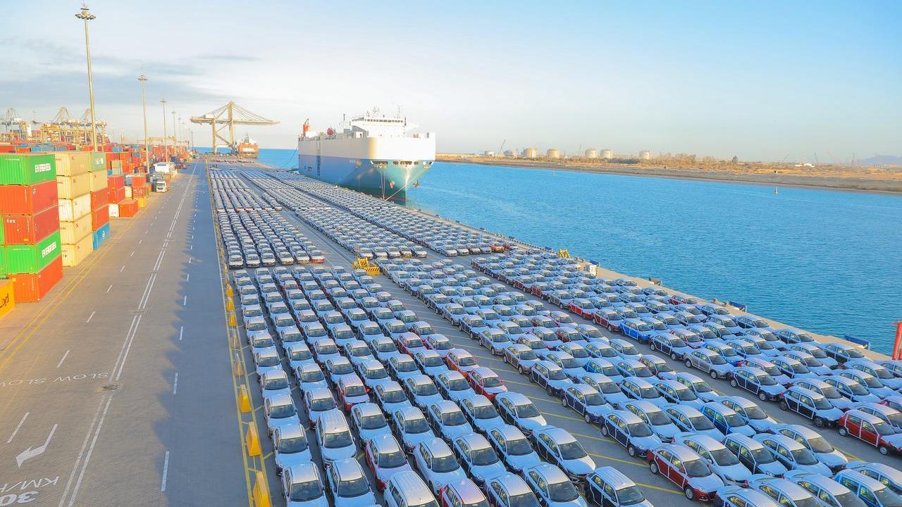 Rows of finished vehicles staged at a port terminal alongside a cargo vessel, illustrating large-scale automotive imports and exports supported by integrated logistics operations.