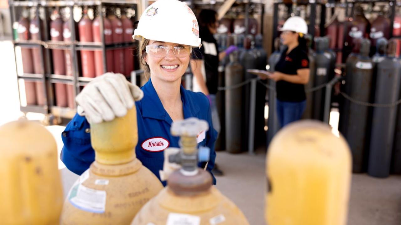 workers in hard hats and protective wear standing with groups of tall metal cylinders.