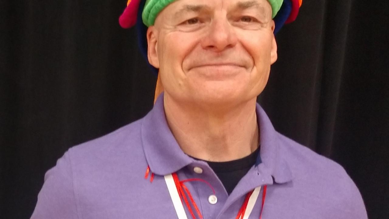 A man in a purple polo and novelty hat holding an award
