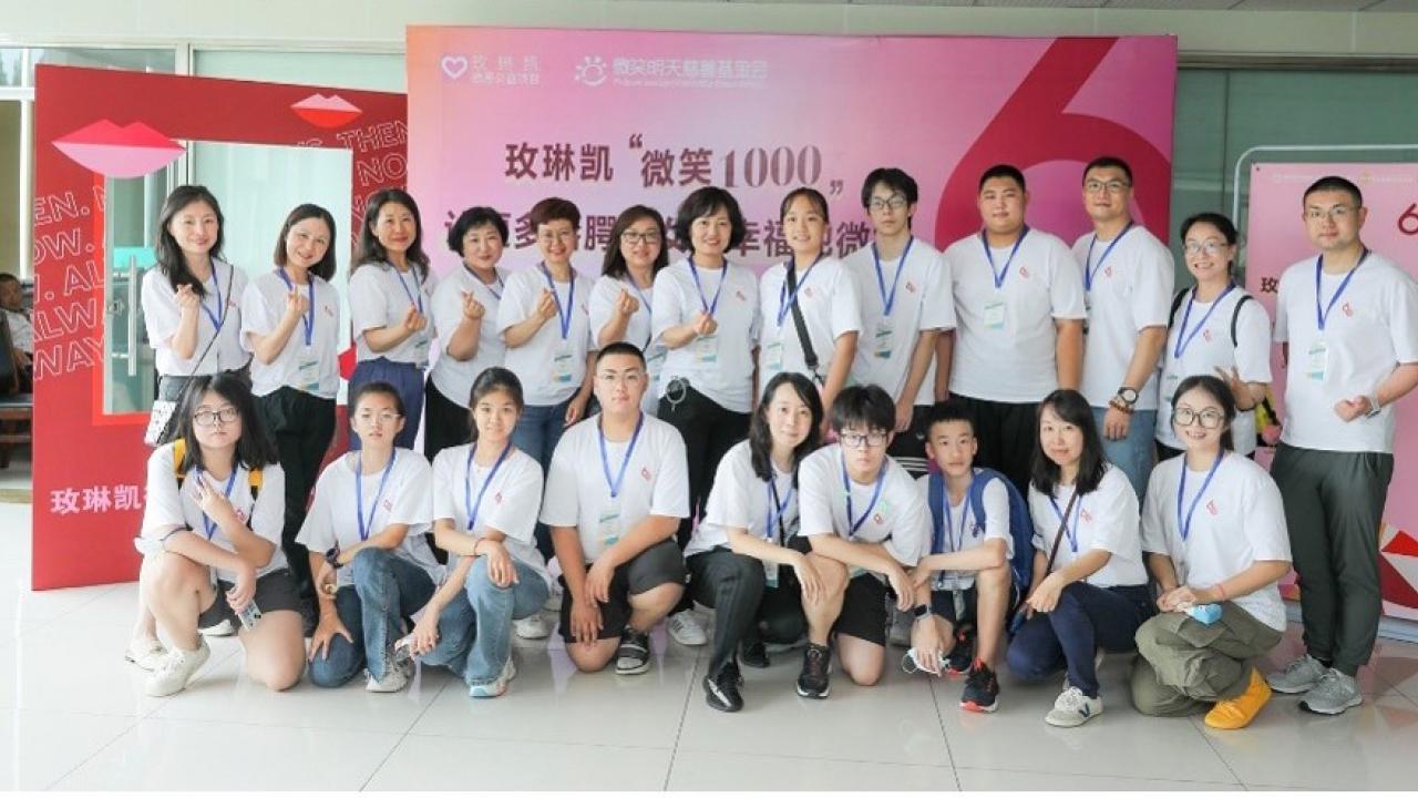 A group of people posed in matching shirts and lanyards in front of a sign in a foreign language.