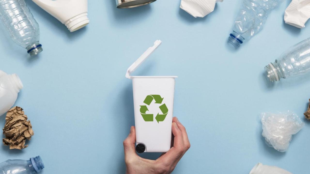 a hand holding a small recycling bin surrounded by plastic bottles