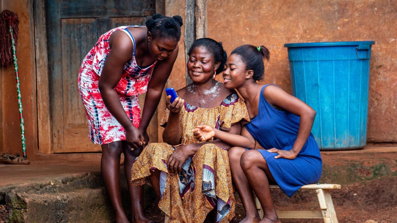 Three women in colorful dresses looking at a blue cell phone