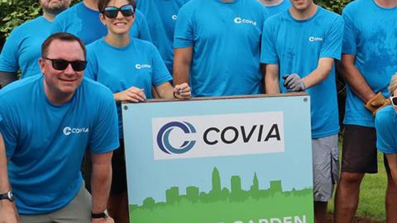 Group of people wearing blue t-shirts gathered around a sign which reads "COVIA CITY SIDE GARDEN"