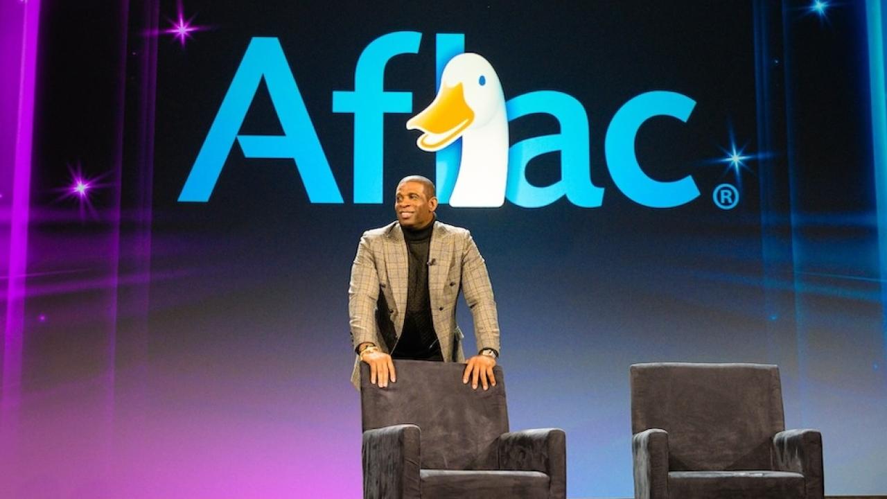 Coach Prime shown on stage with the Aflac logo.