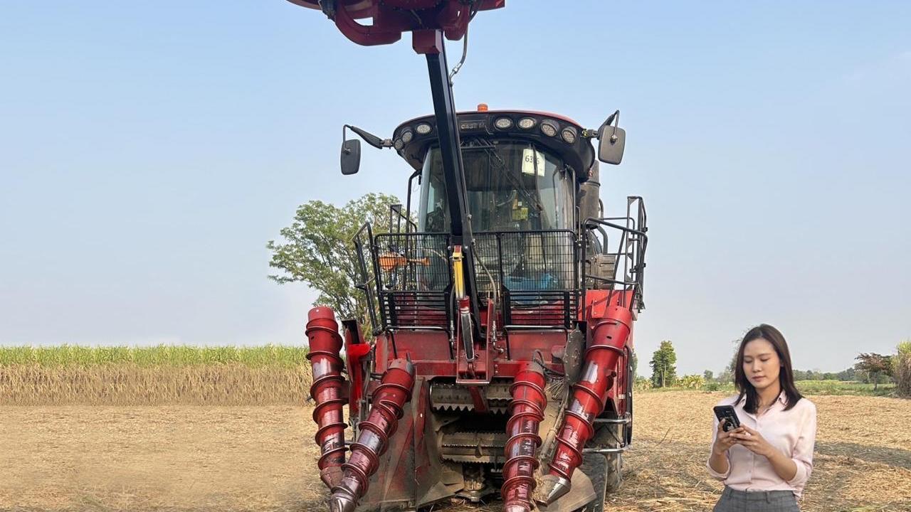 A red piece of agricultural equipment in a crop field, with a person stood to the right 
