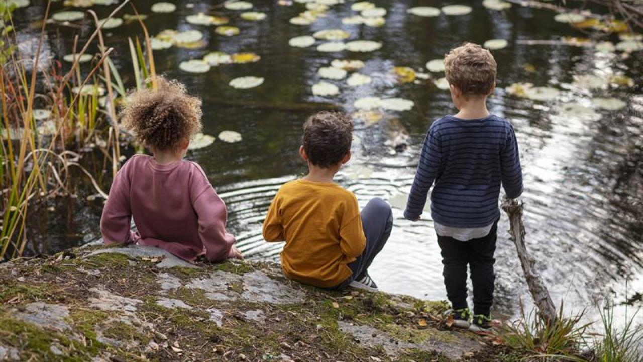 Three children sitting by a stream.