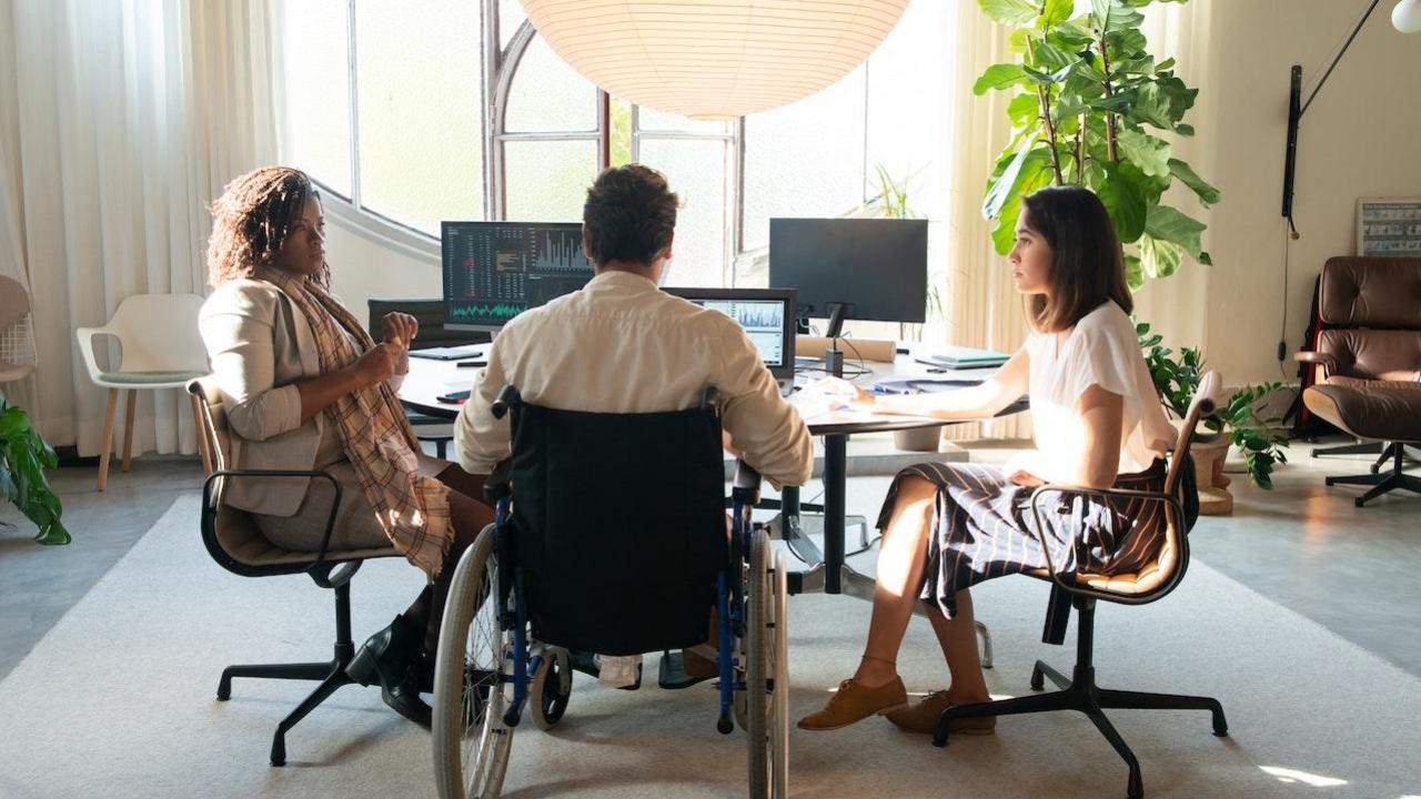 Three people working at a table together. One is in a wheelchair.