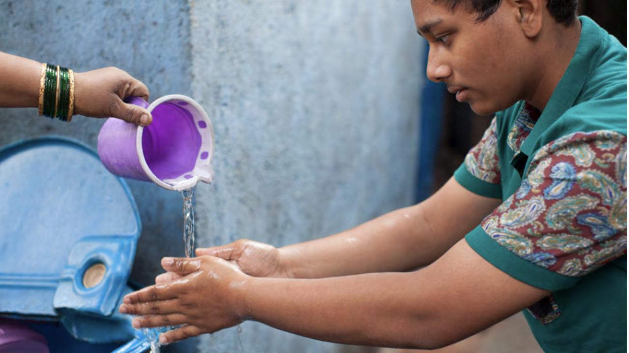 Young person having water poured over his hands so that they can wash them.