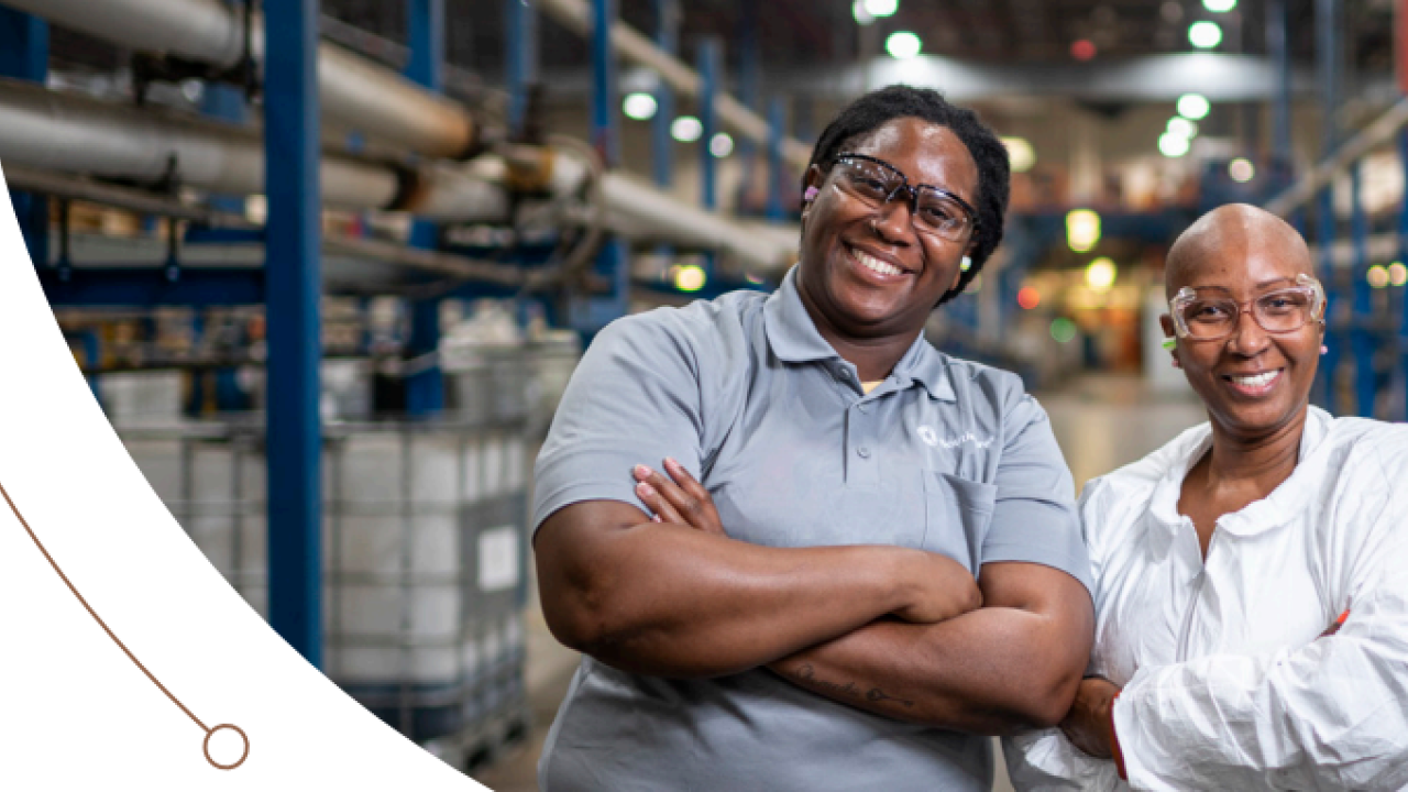Two smiling people with arms crossed in a manufacturing environment.