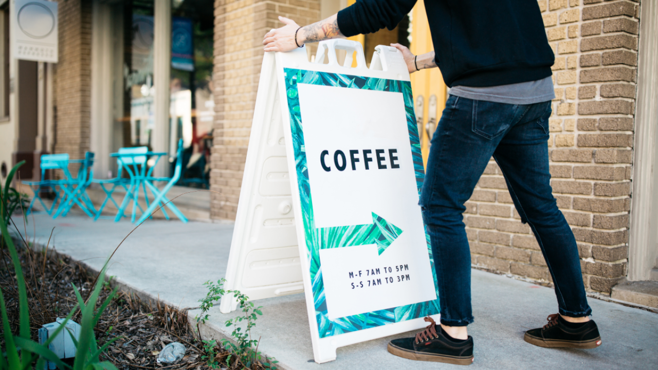 Person shown adjusting a sign in front of a coffee shop.