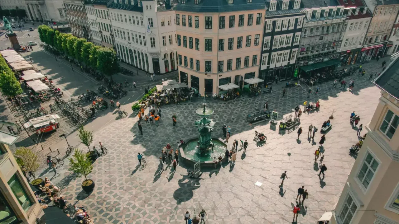Aerial view of a city center full of pedestrians and bicycles. A fountain central to the street crossing.