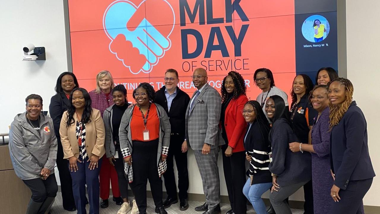 A group of people stood together in front of a projector board that reads "MLK DAY OF SERVICE"