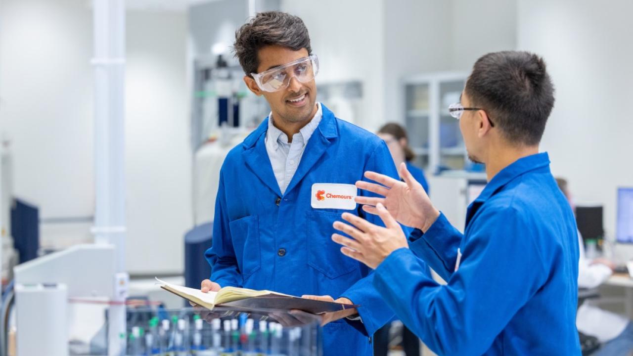 Two people wearing blue lab coats in a lab
