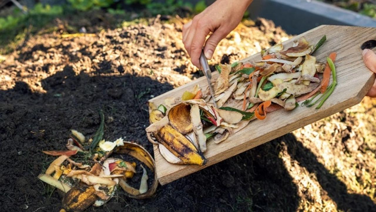 Someone scraping food waste off a cutting board into a compost pile