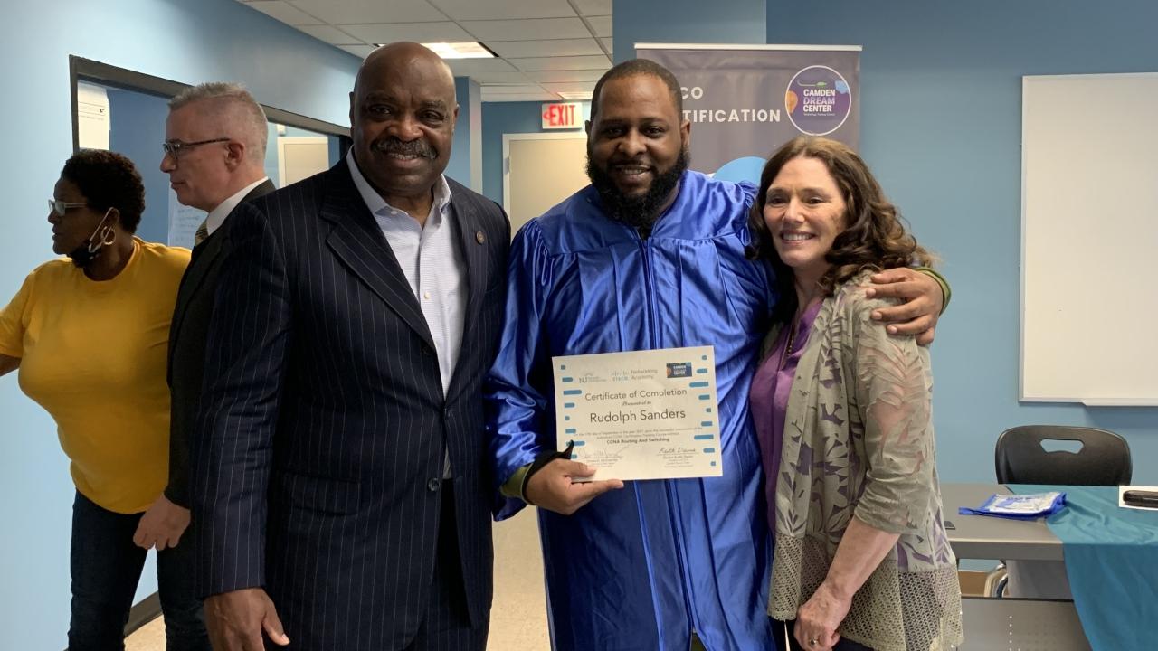 a group of three people, the central holds up a certificate with their other arm around the person on the right