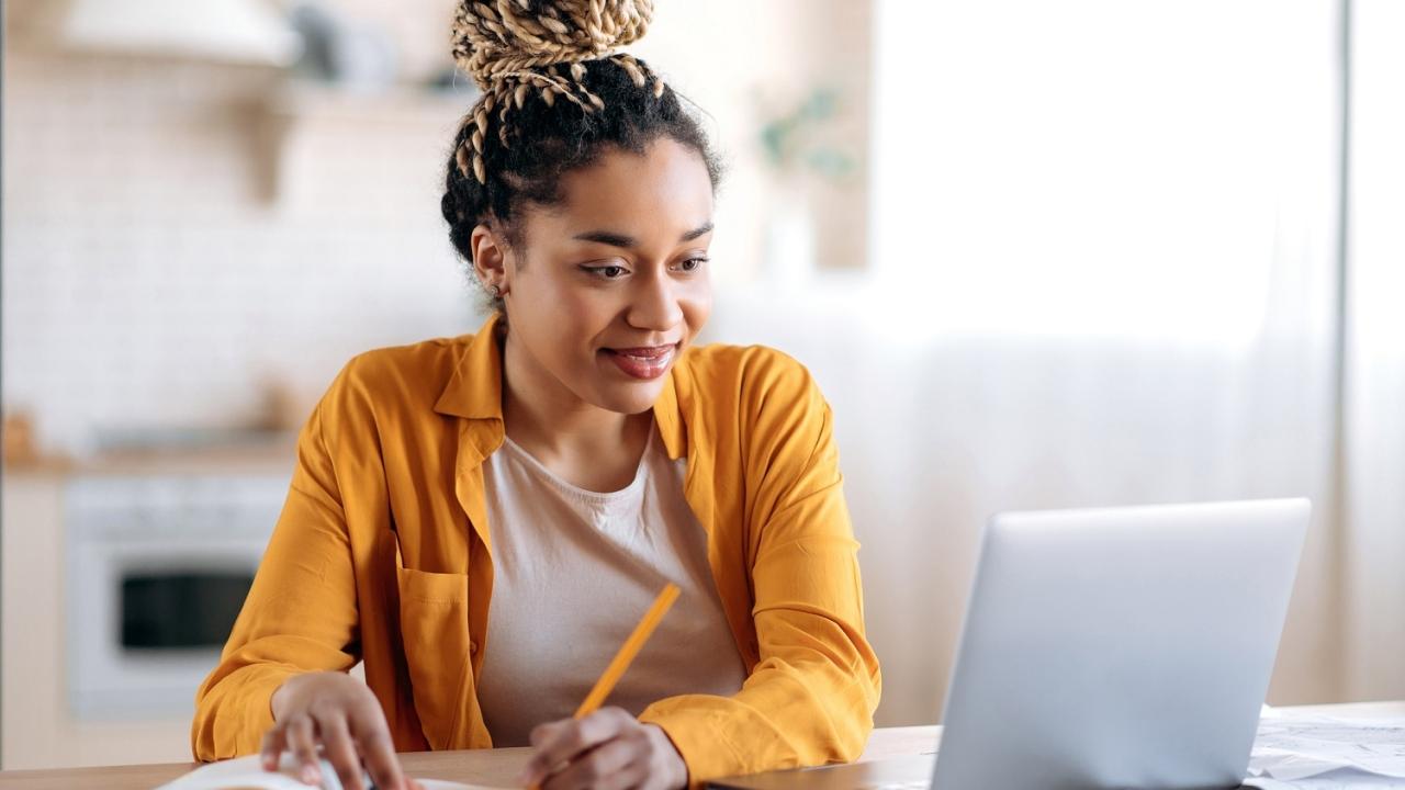Person writing in notebook while looking at laptop screen