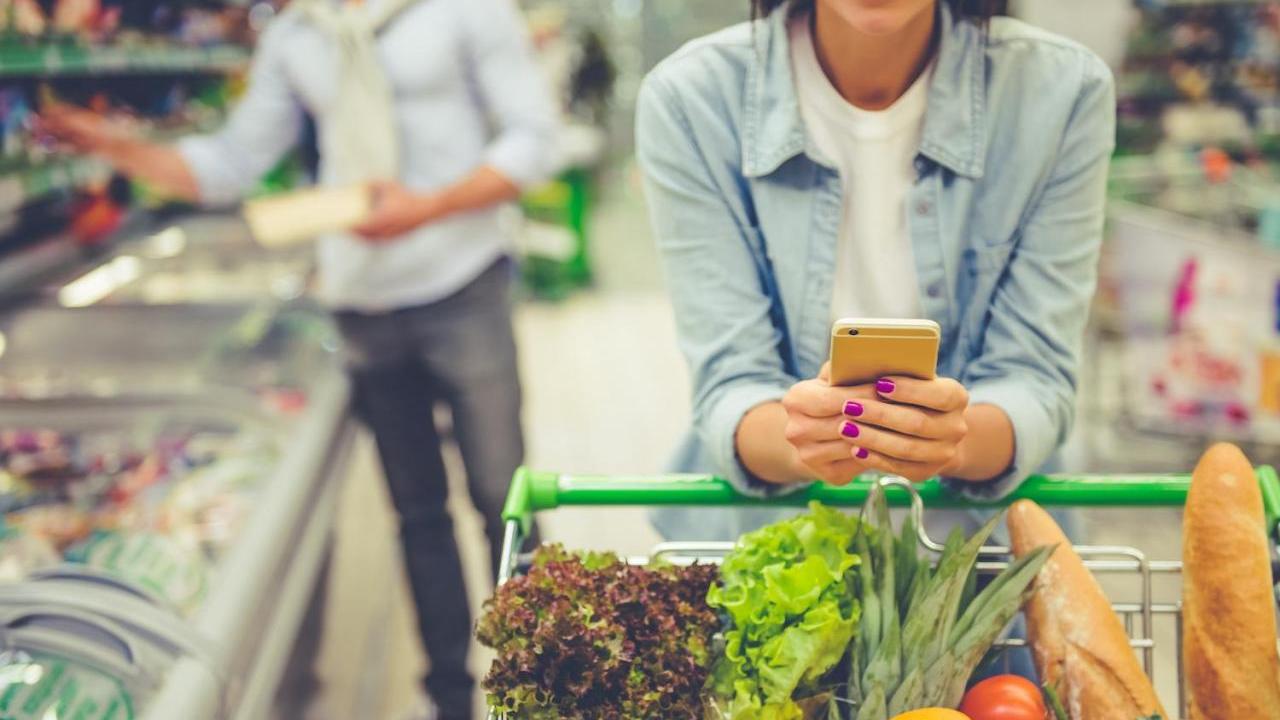 A couple shopping in a grocery store. One of them is consulting their phone.