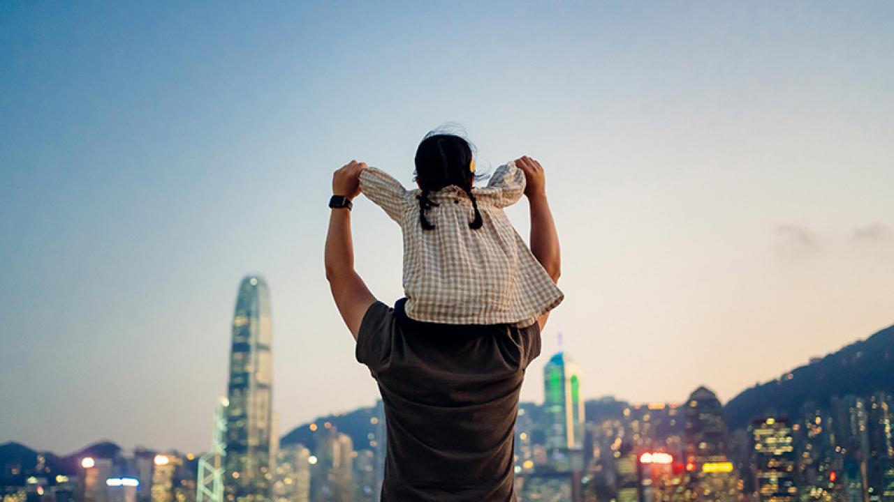 person holding small girl on shoulders in front of skyline