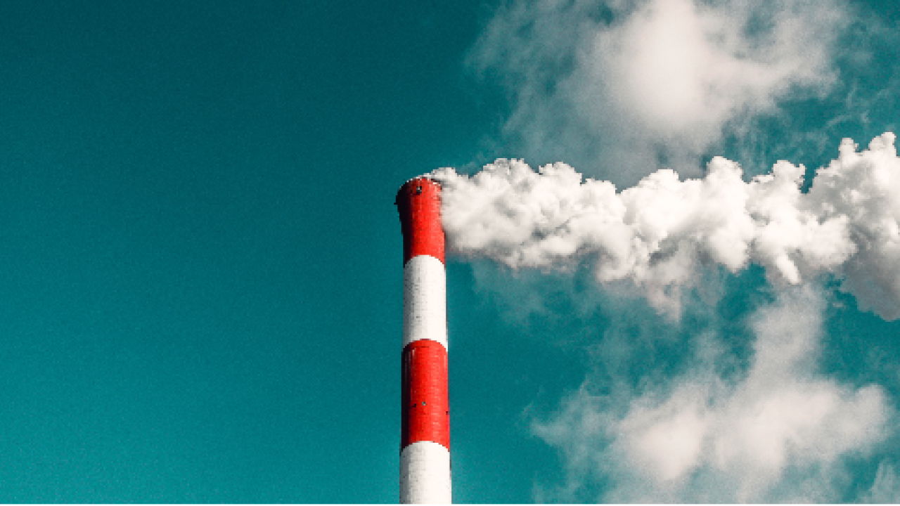 Red and white smokestack billowing smoke against a blue sky.