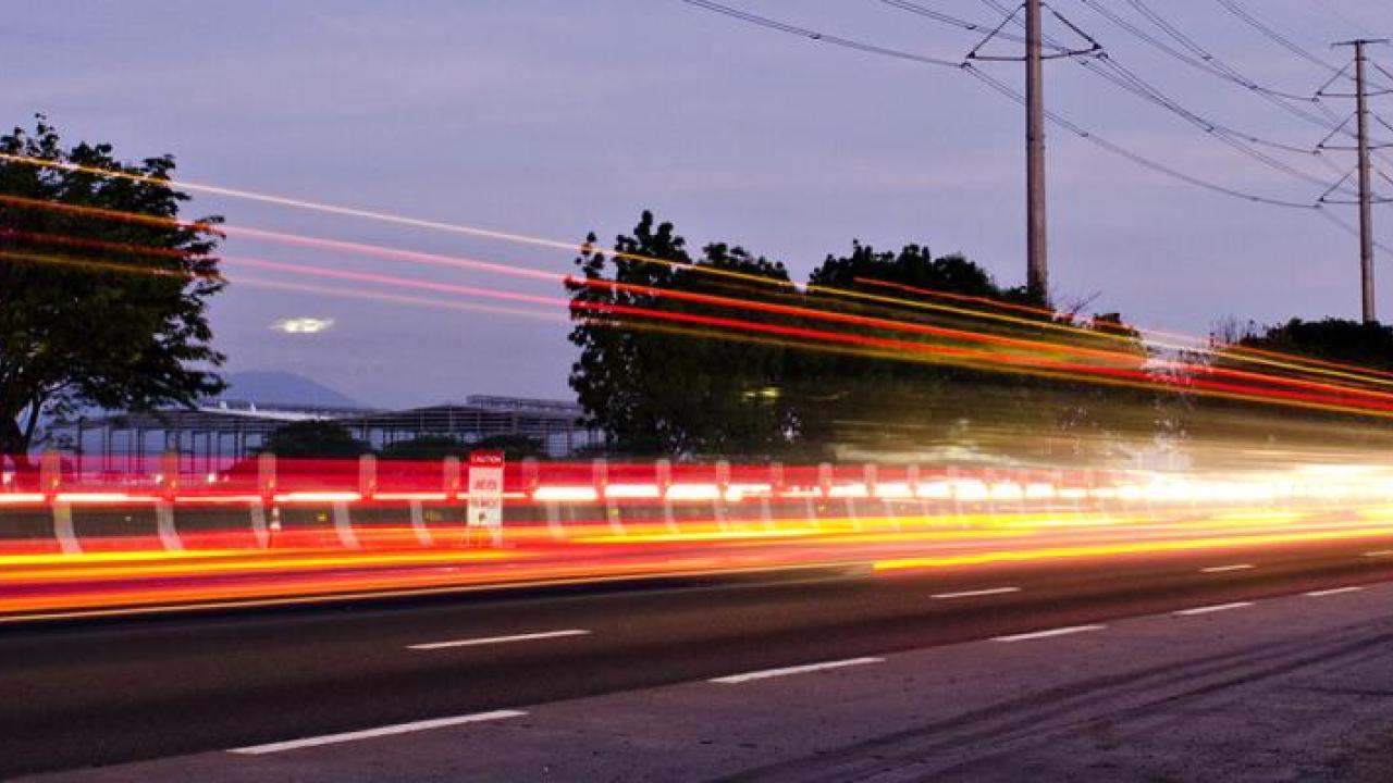 Long exposed lights from a vehicle on a road, power lines along the side of the road.