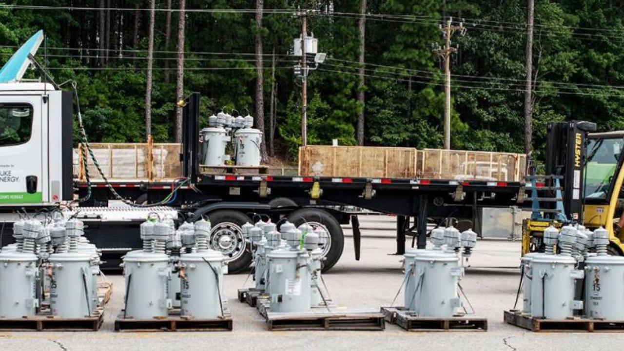 A semi truck in a parking area. Electrical equipment and a person in a forklift in front of it.