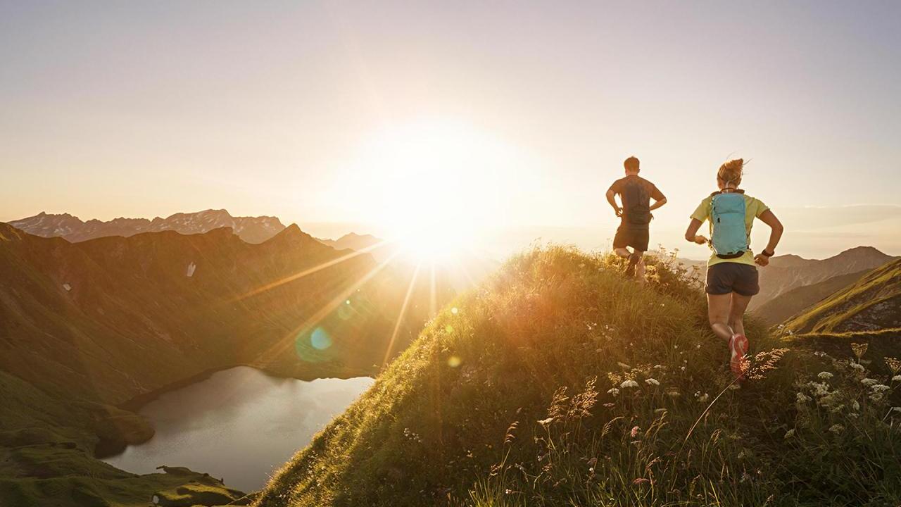 Photo of the sun setting with two people running on some hills 