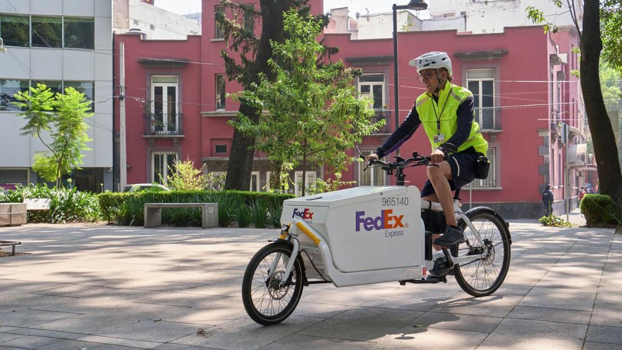 Person riding a FedEx bike outside with buildings and tree's behind them