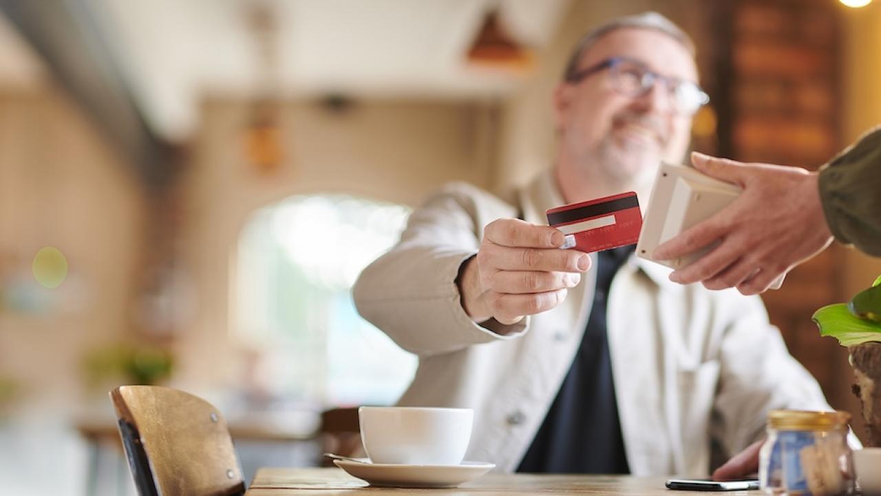 A man shown having coffee and paying with a credit card.