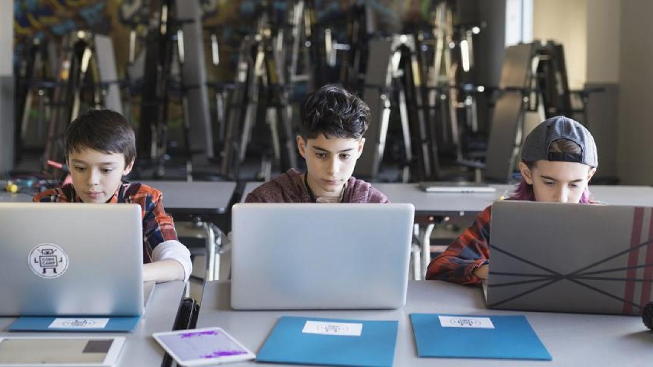 Three students at a shared table each with an open laptop.