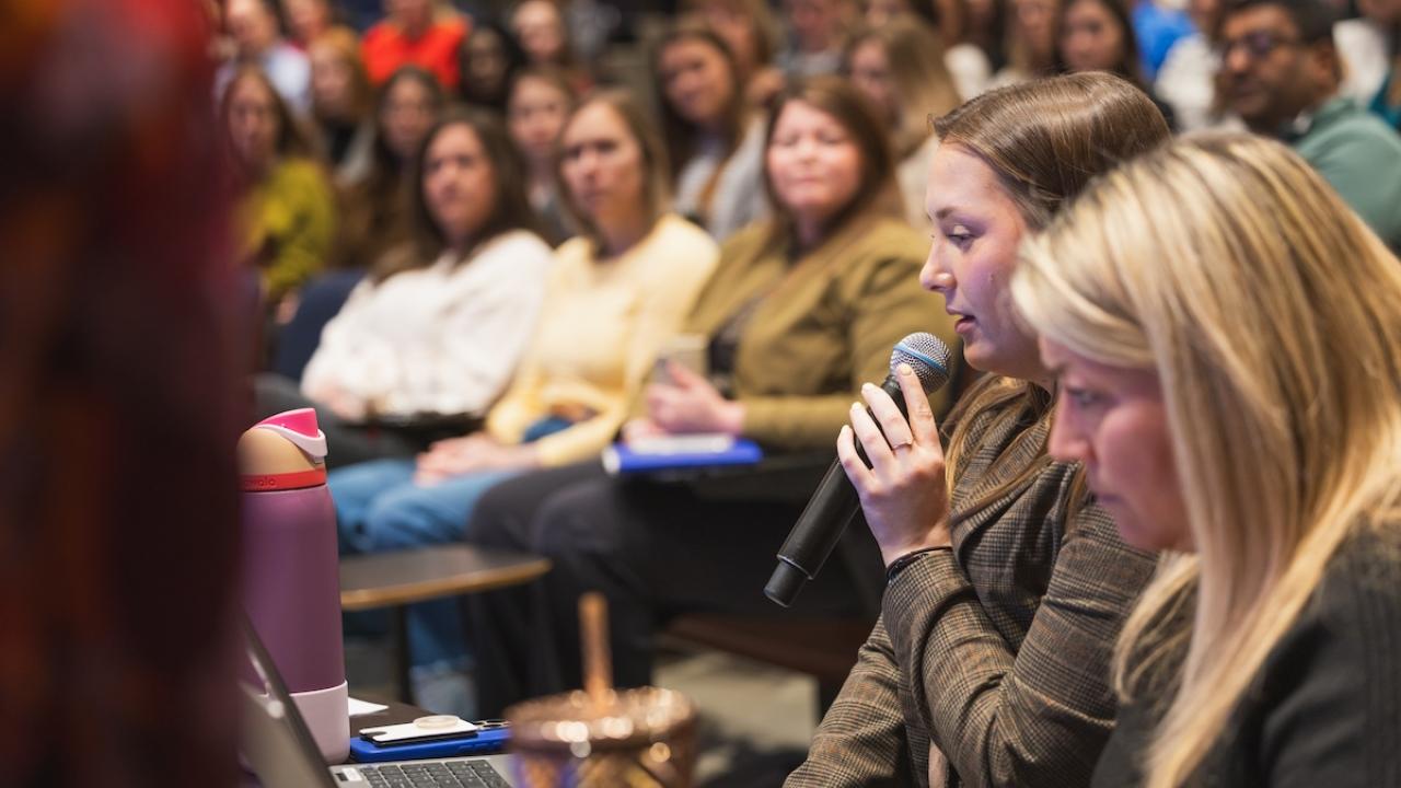 Two people speaking from a podium to a group of people.