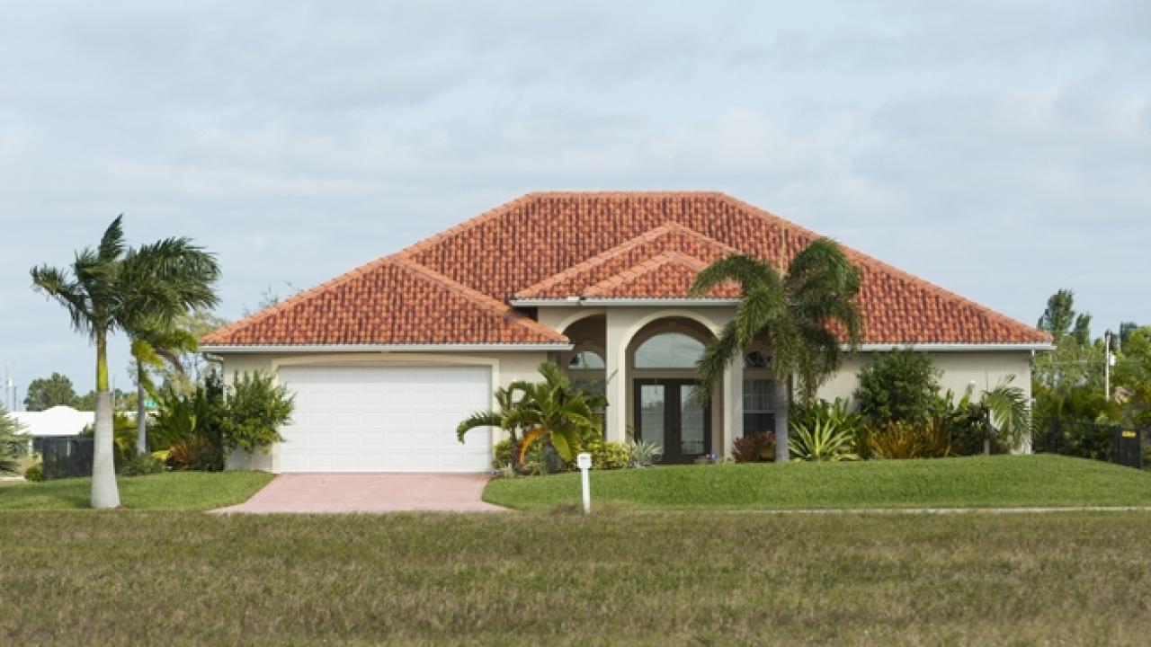 Palm trees and lawn in front of a stucco house with a red tiled roof.