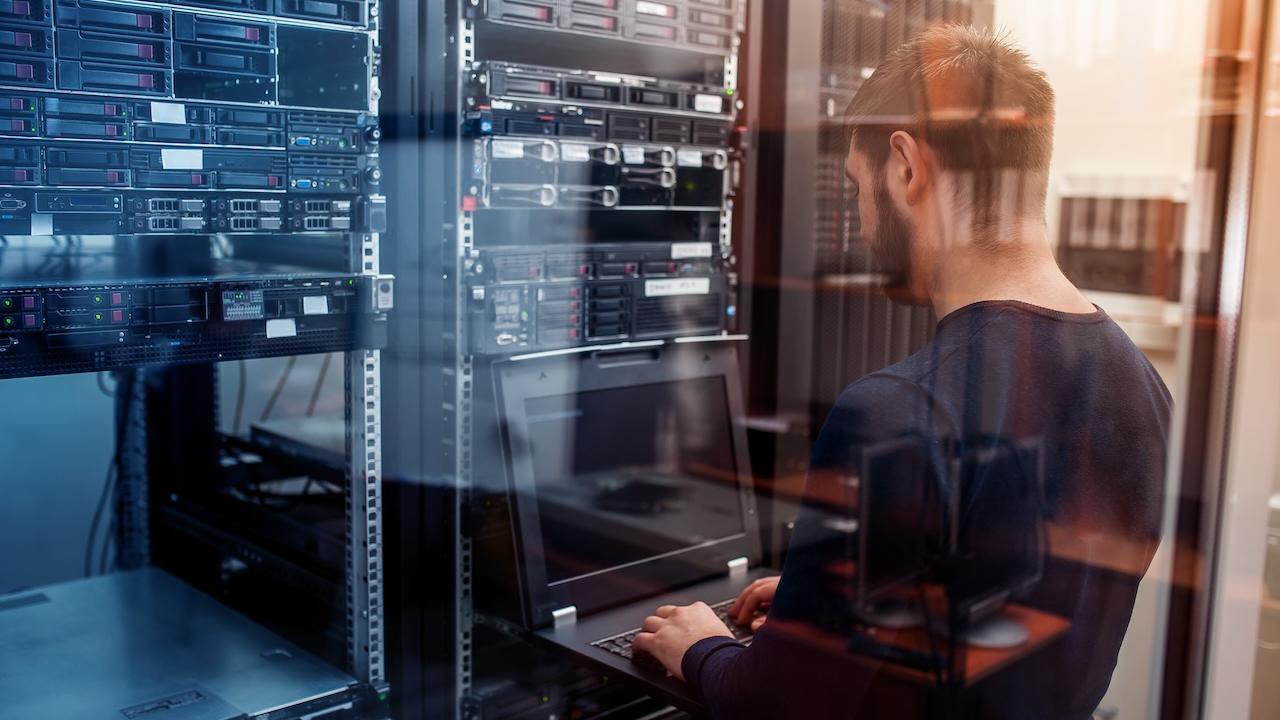 A person with a laptop working in a server room.
