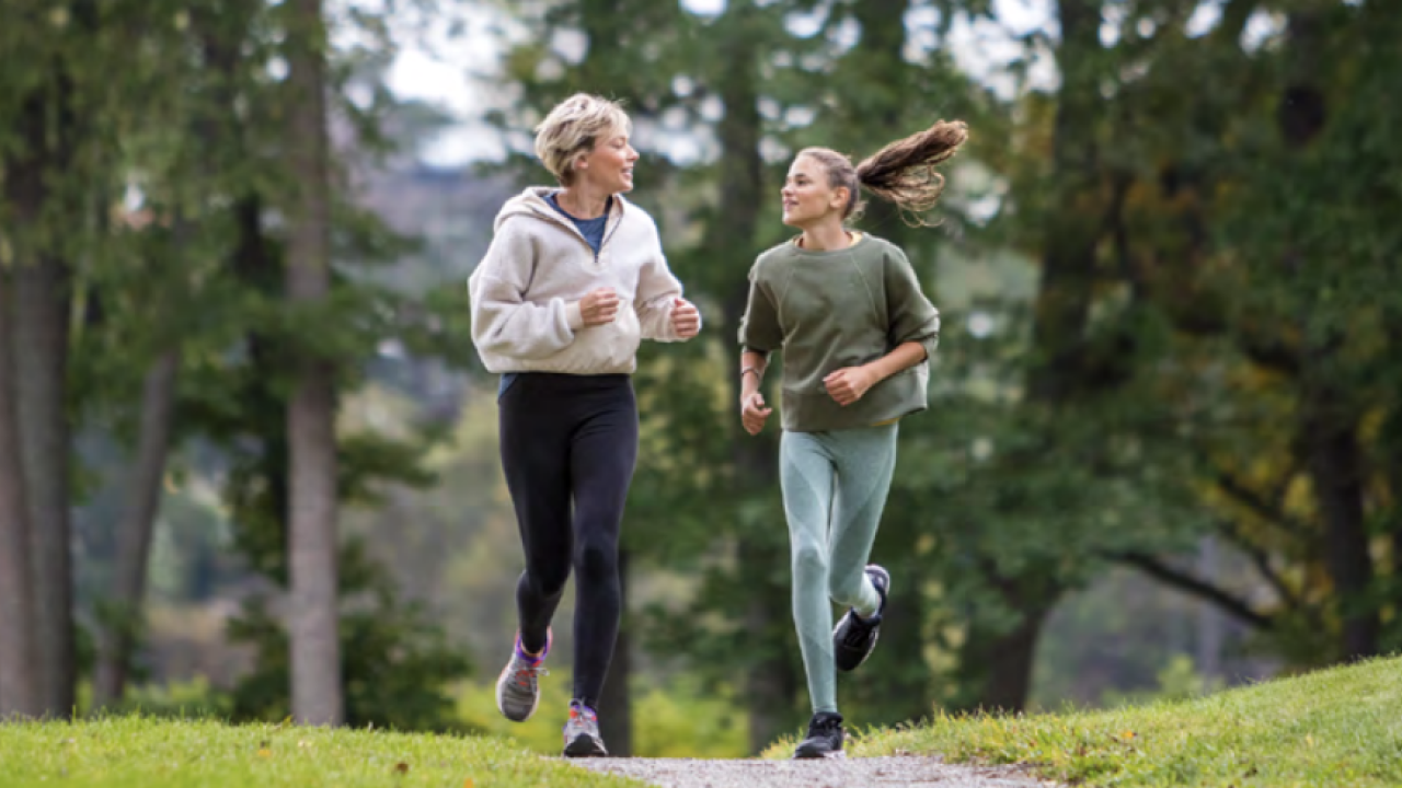 Two women jogging on a path on the edge of a forest.