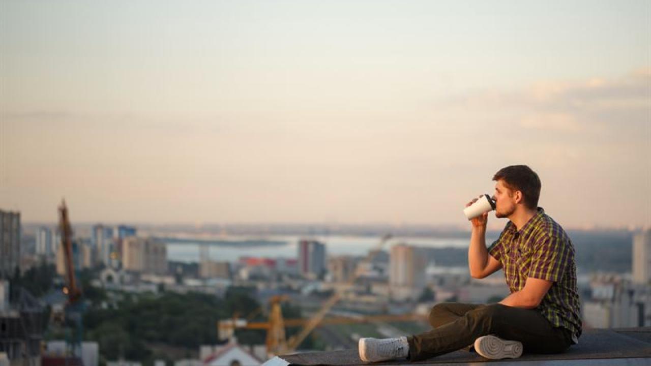 Man sitting on a rooftop drinking from a paper cup.
