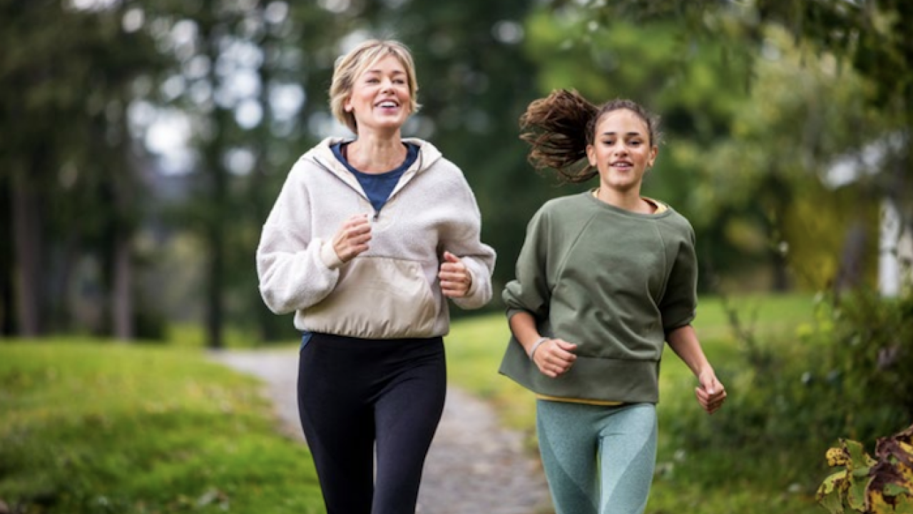 Two women running in a park with trees and grass.