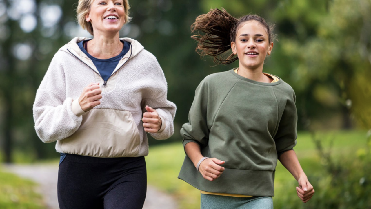 A mom and her daughter jogging on a path.