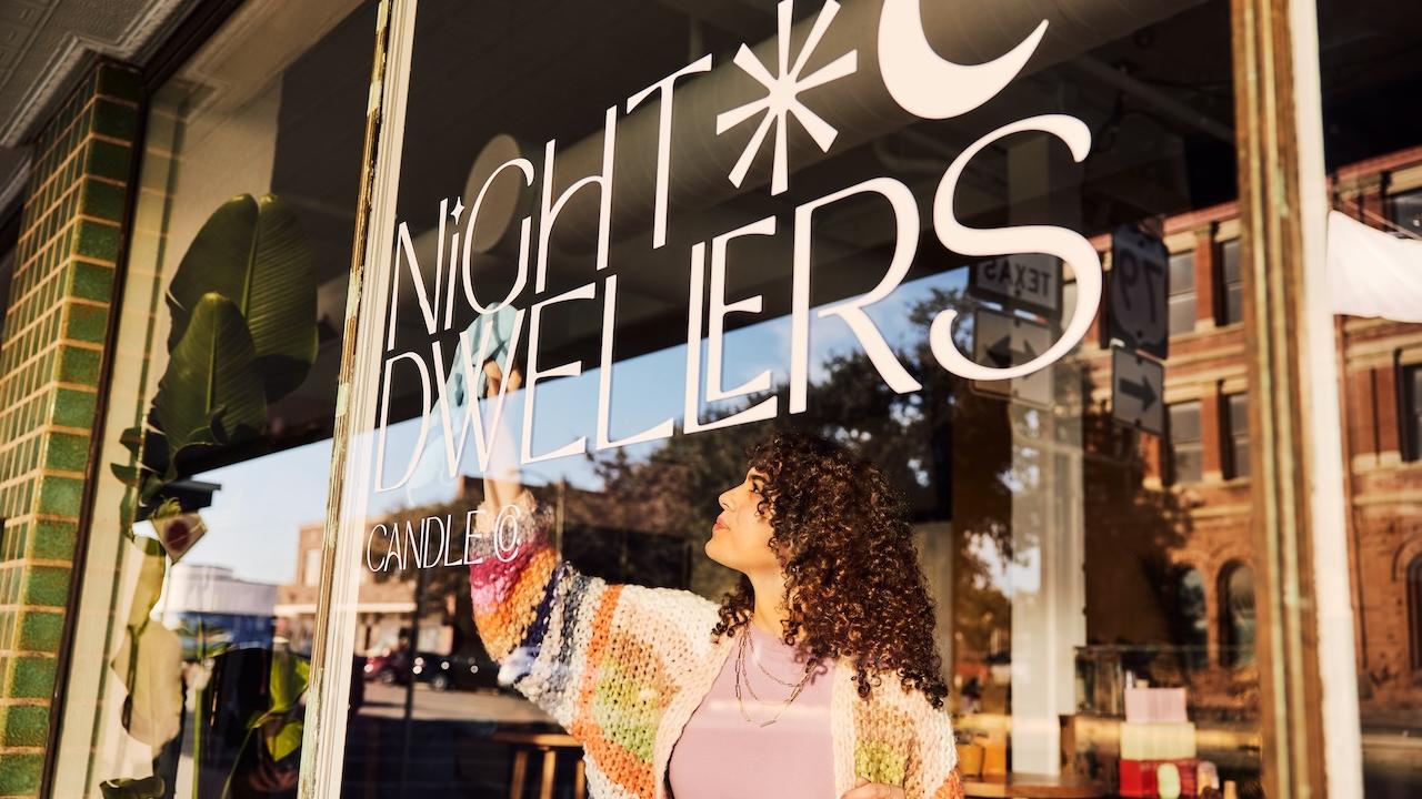A person cleaning a window of a store called Night Dwellers.