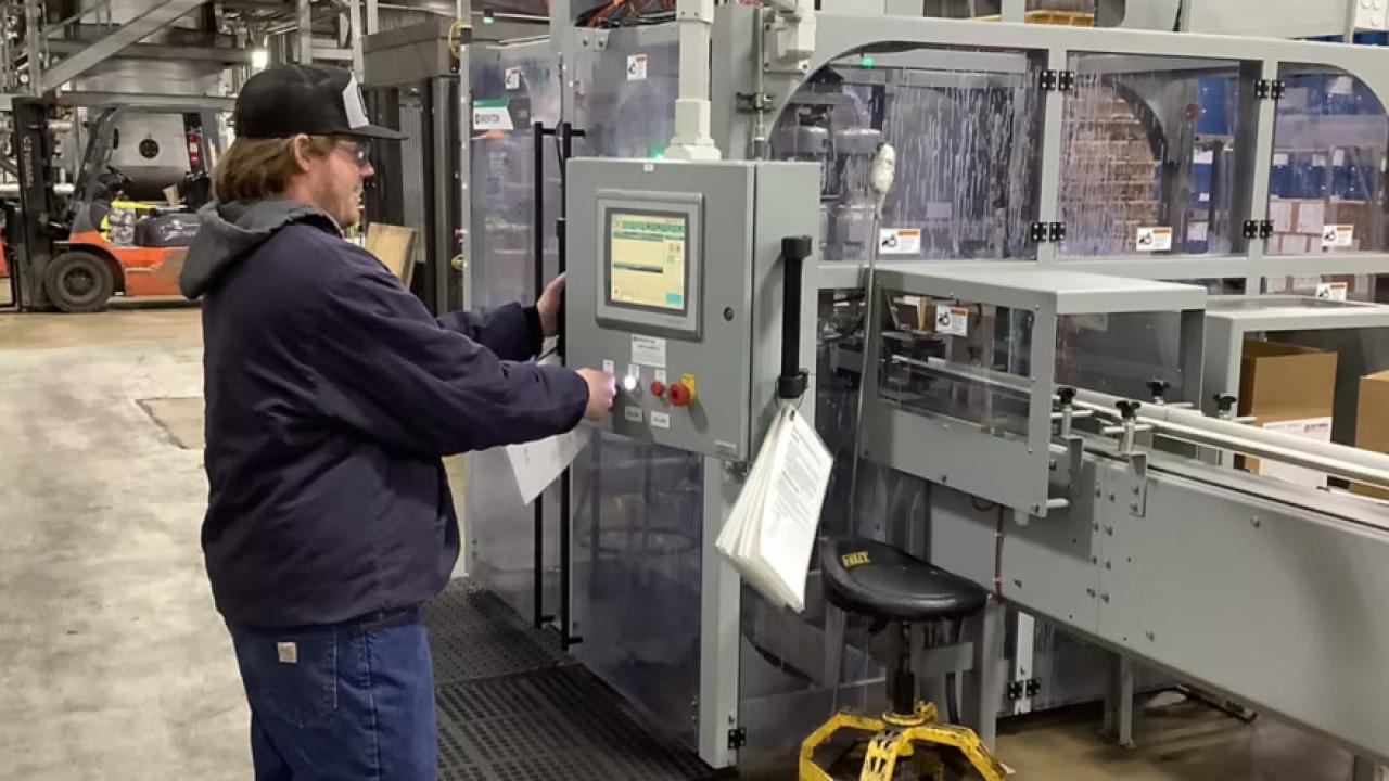 A person pushing a button on a box on front of a large CNC type machine.