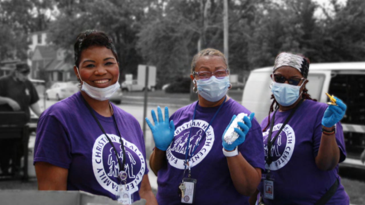 three people in protective masks and gloves outside. Each wearing a Family Christian Health Center tshirt.