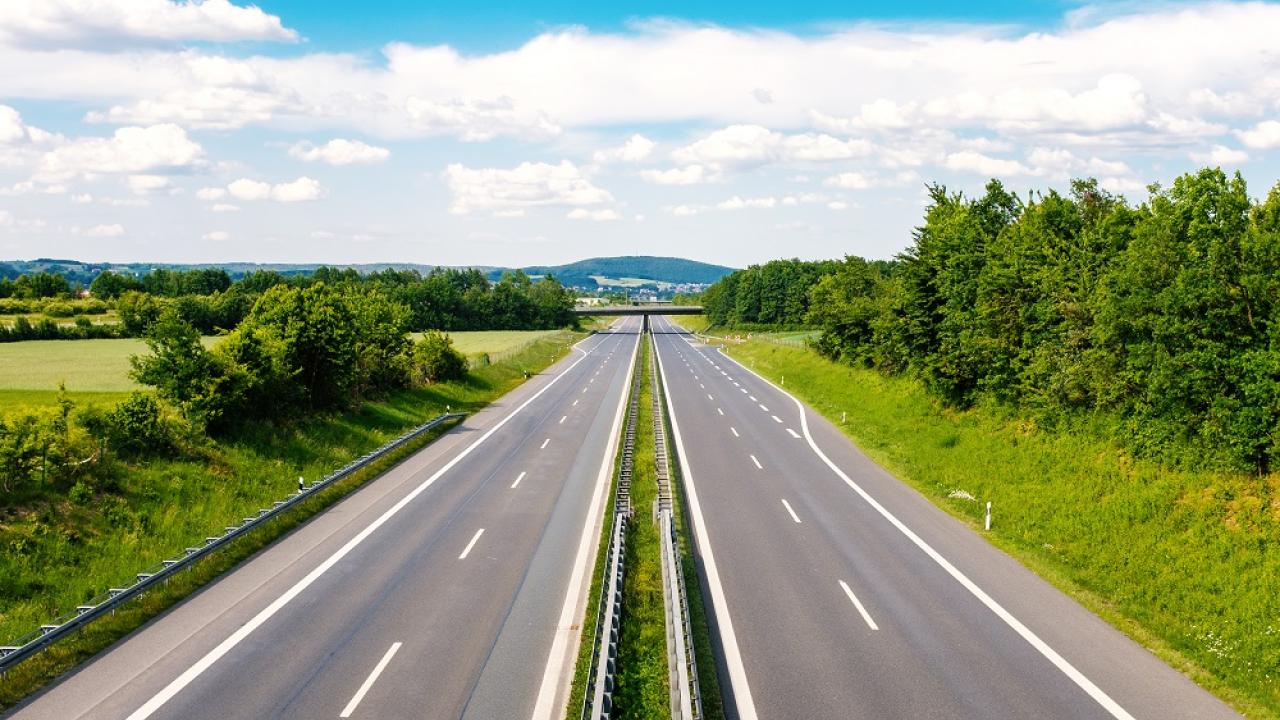 A road stretching off into the distance under a sunny sky with green grass and trees on either side