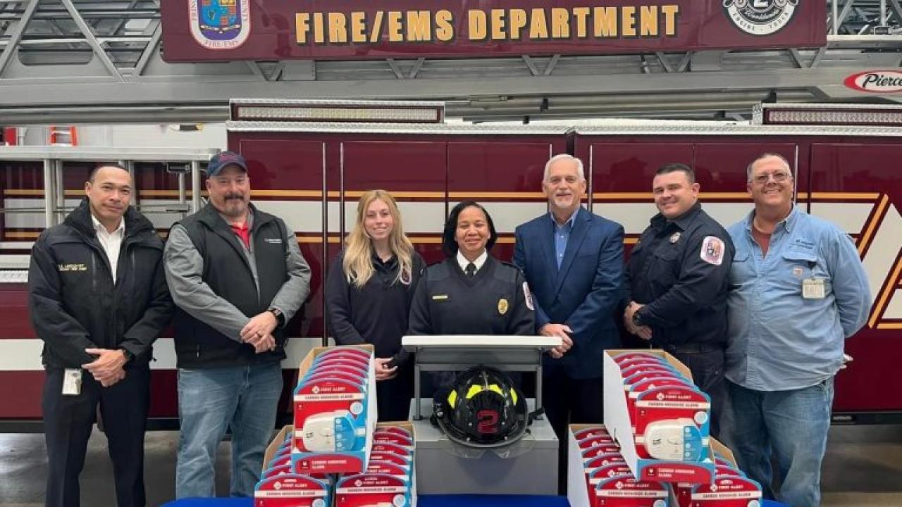 A line of people standing in front of a fire truck with a banner "Prince George's county fire/ems department". A table with smoke detectors in front of them.