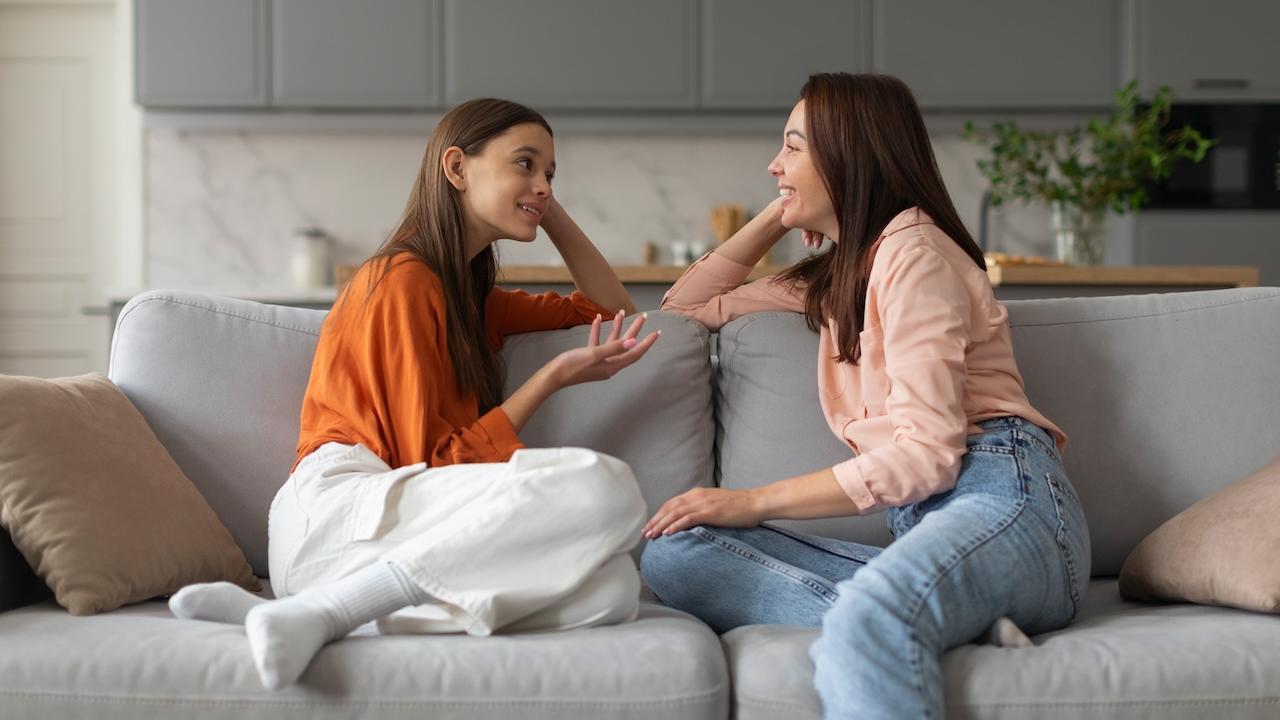 A mom and her daughter having a chat while sitting on a couch.