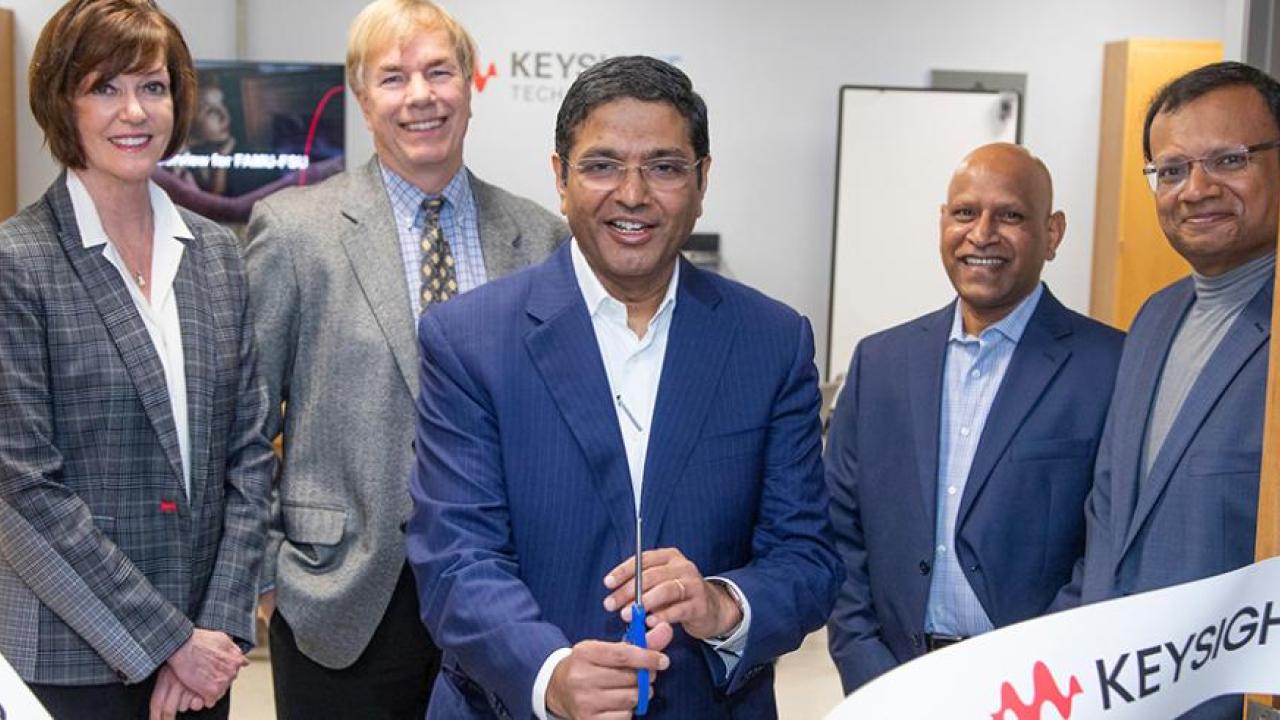 Five people in a door way, the middle person holding scissors having just cut a ribbon with Keysight logos on it.